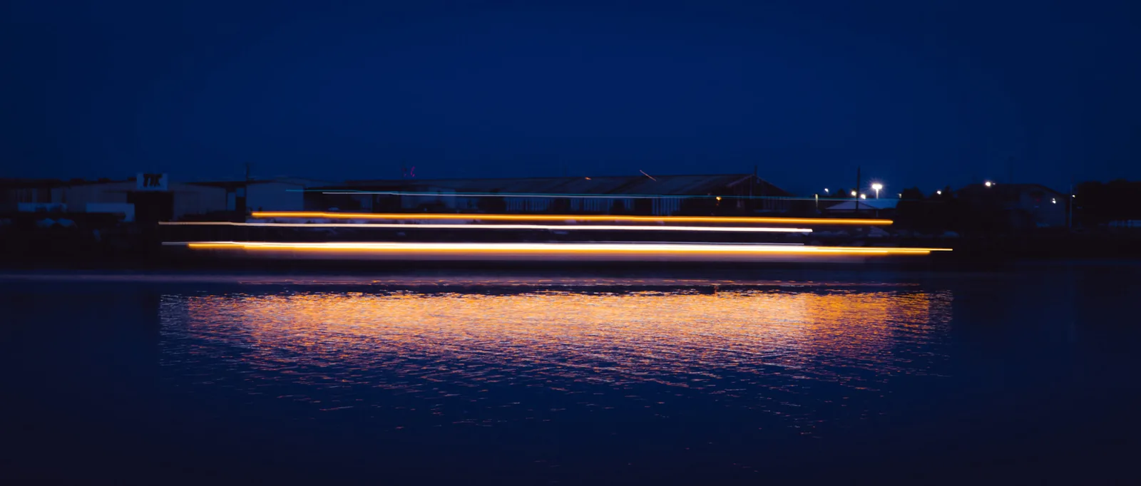 Boat lights streak across the Savannah River at night in a long-exposure photo from the waterfront.